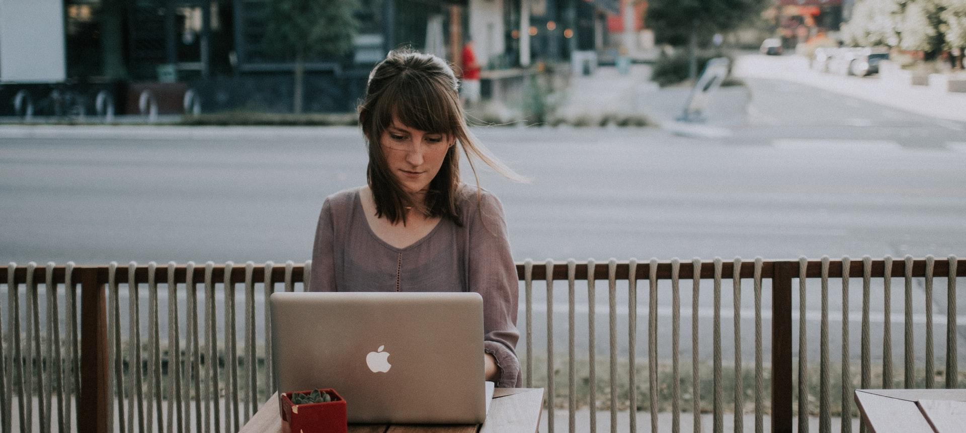 woman in gray shirt sitting on bench in front of MacBook
